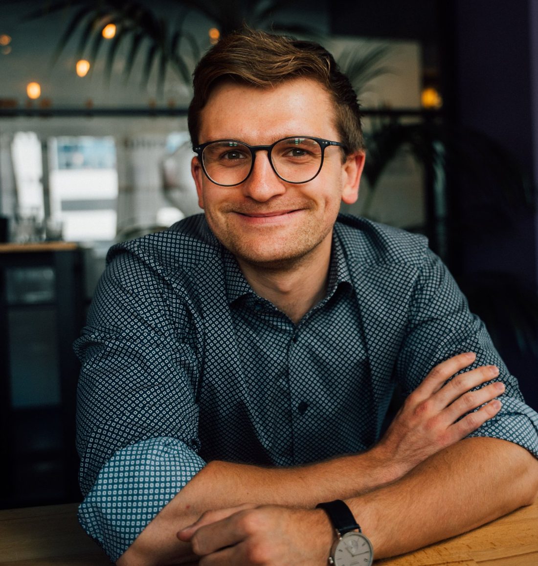 Lukas Honemann sitzt lächelnd an einem Holztisch